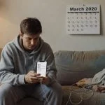 Person at home during COVID-19 pandemic using smartphone connected to charger while on video call, lockdown lifestyle