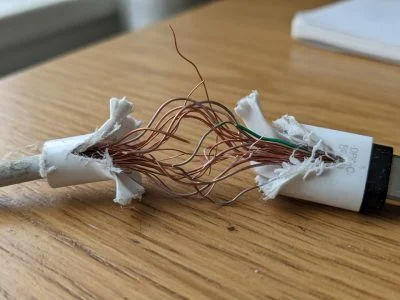 A frayed USB-C charging cable with exposed copper wires near the connector, resting on a wooden desk