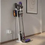 Cordless stick vacuum cleaner on a wall charging dock in a modern home hallway with a USB charge limiter attached